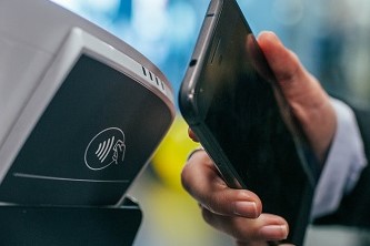 A person making a payment to a contactless card reader using their black smartphone
