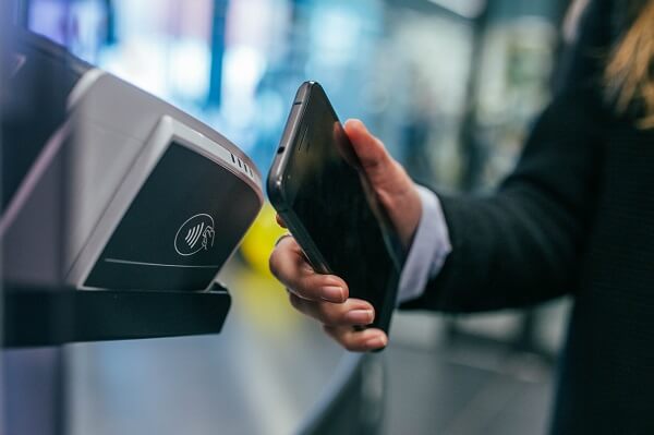 A person making a payment to a contactless card reader using their black smartphone