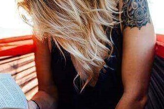 A woman with a tattoo on her shoulder reading a book outside