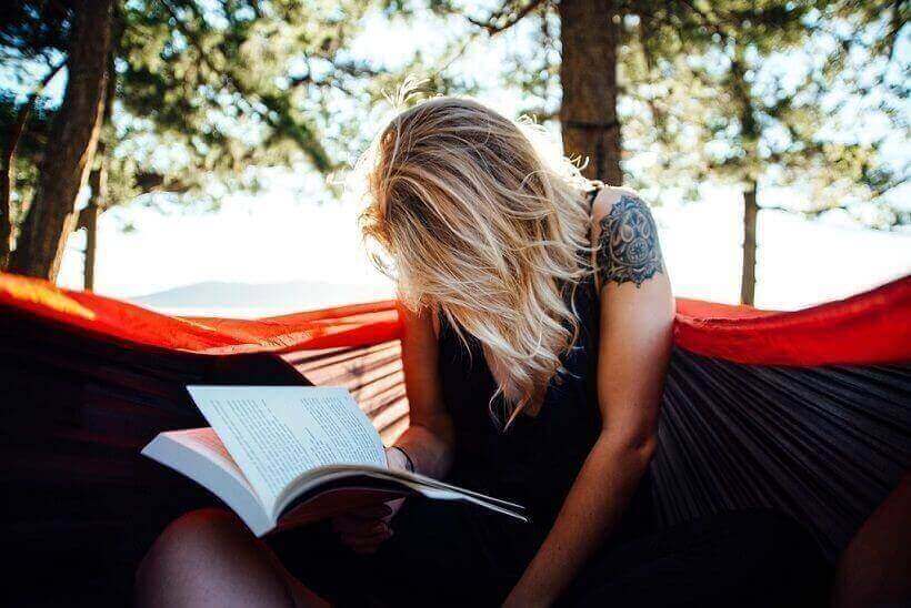 A woman with a tattoo on her shoulder reading a book outside