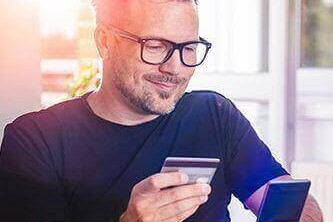 A man sitting in front of a laptop, using his credit card for a transaction on his phone