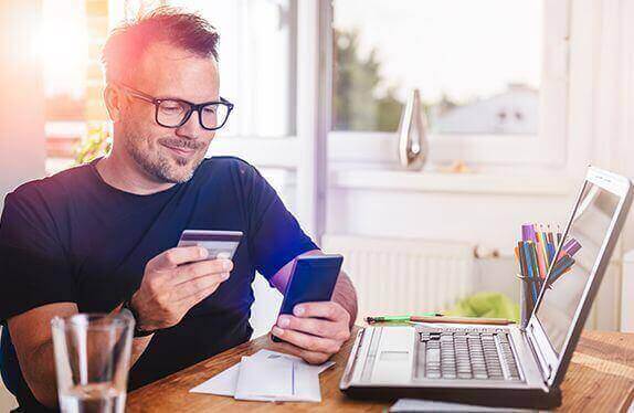 A man sitting in front of a laptop, using his credit card for a transaction on his phone
