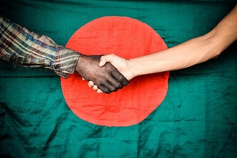 An image of two people shaking hands with the Bangladesh flag in the background