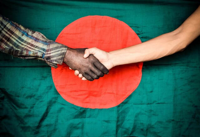 An image of two people shaking hands with the Bangladesh flag in the background