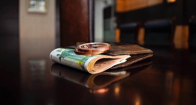 A bundle of currency bills and a coin placed in a wallet lying on a table