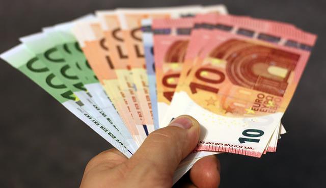 A person holding Euro currency bills of various denominations in their hand