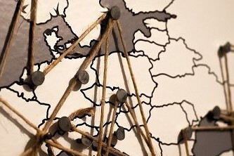 An image of a sepia toned map of Europe, with pins pushed into several countries and a string woven between the pins