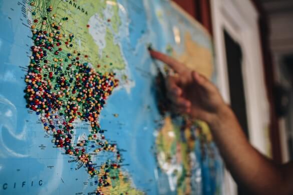 A person pointing on a map that has pins on it for various countries