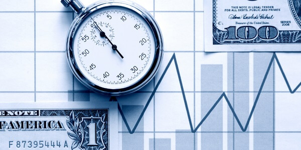A clock on top of a line graph and a couple of US Dollar currency bills