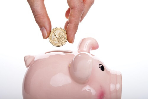 A hand putting a coin in a pink piggy bank