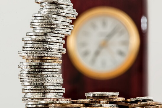 A stack of gold and silver coins with a clock in the background