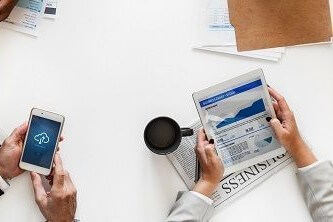 Four people using mobile phones on a desk with financial forms, papers and newspapers lying around