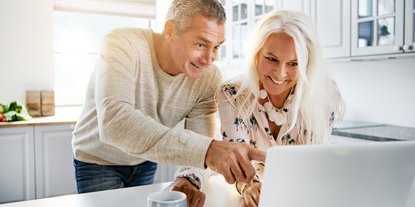 An image of a happy couple looking at something on their computer in their kitchen