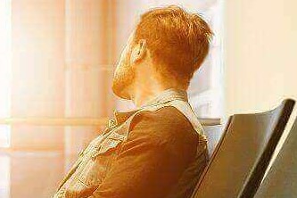 A man sitting on gang chair at the airport with feet propped up on his luggage, looking at airplane taking off