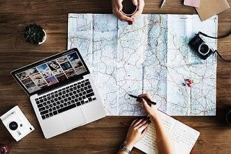 Top-view photography of persons holding mug and pen using MacBook and world map