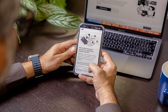 An image of a person using a payment app on their cellphone with a laptop in the background