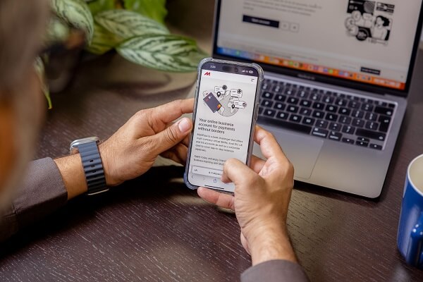 An image of a person using a payment app on their cellphone with a laptop in the background