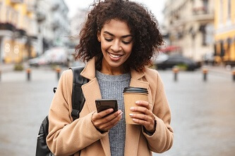 A happy woman using her cellphone with a coffee cup in the other hand