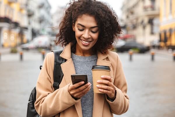 A happy woman using her cellphone with a coffee cup in the other hand