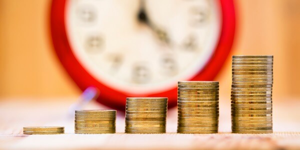 Stacks of coins in increasing order with a clock in the background