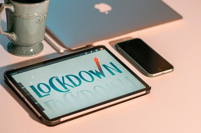 A silver iPhone 6 beside an iPad and a MacBook with the word lockdown displayed on the iPad