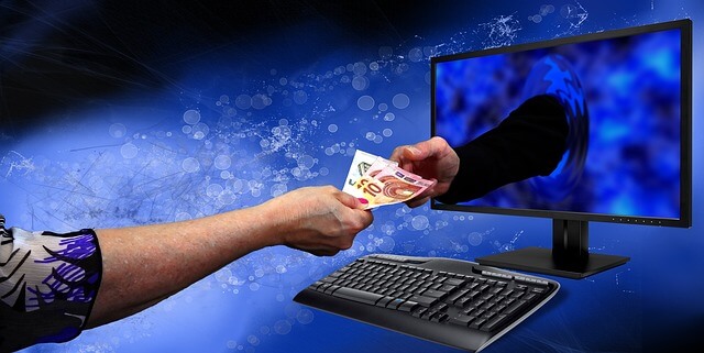 An image portraying a fraudulent transaction with 2 hands exchanging money across a computer monitor
