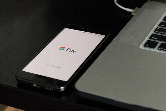 Black Android smartphone next to an Apple Mac laptop with Google Pay application