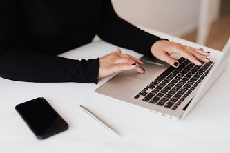 An image of person sitting on a table and using a laptop, with a mobile phone lying on the table