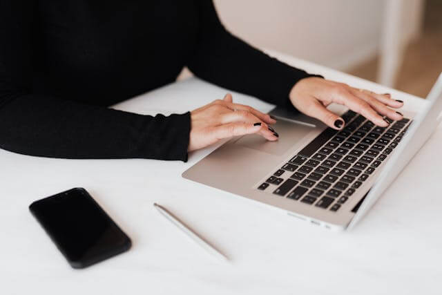 An image of person sitting on a table and using a laptop, with a mobile phone lying on the table