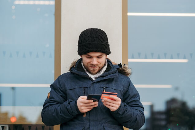 Cheerful man entering details of credit card on smartphone on street