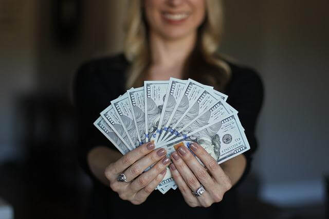 A happy woman holding US Dollar bills in a fan formation