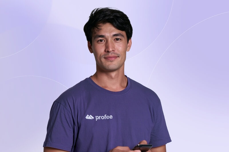 An image of a smiling young man with a Profee t-shirt on and a mobile phone in hand
