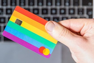 A person holding yellow and pink card with a Mac laptop in the background