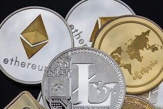Several different cryptocurrency coins in a pile on a black background