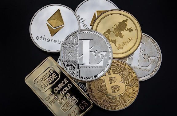 Several different cryptocurrency coins in a pile on a black background