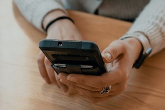 A person sitting at a desk and using a black mobile phone
