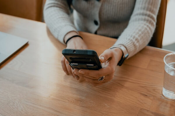 A person sitting at a desk and using a black mobile phone