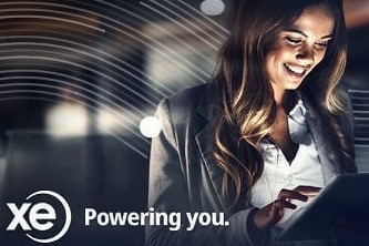 An image of a smiling woman in professional attire using a tablet with XE Money Transfer logo in the background