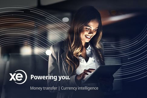 An image of a smiling woman in professional attire using a tablet with XE Money Transfer logo in the background